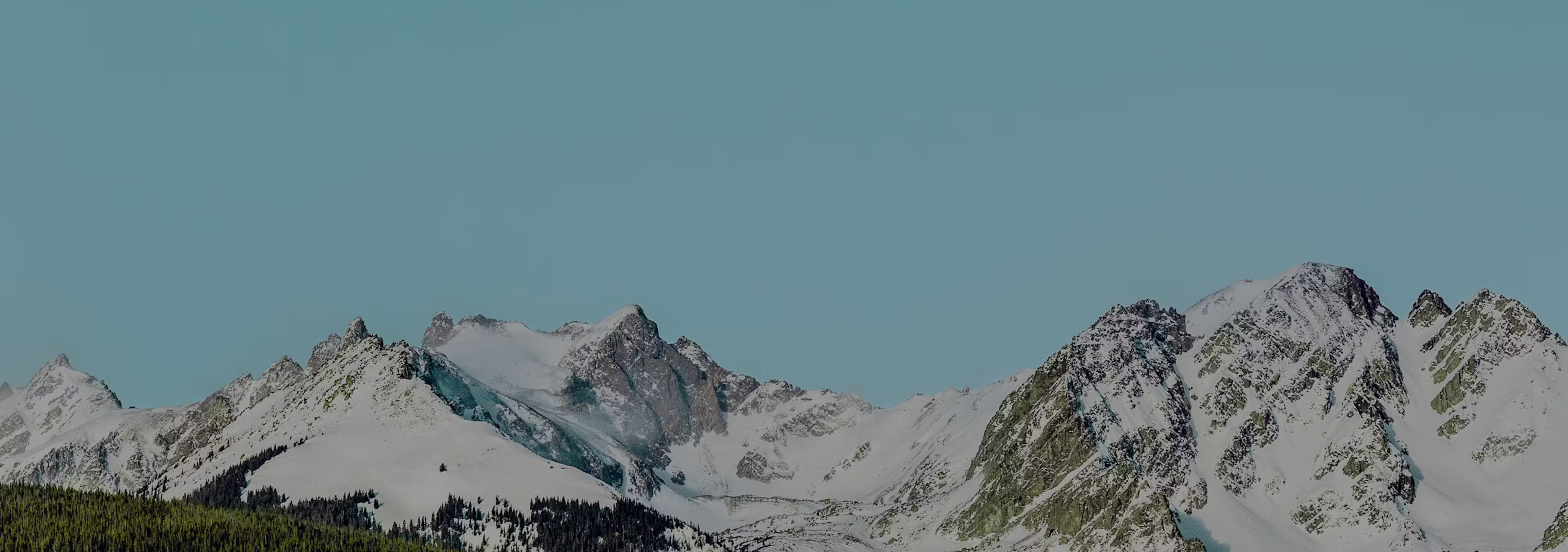 Alpine mountain peaks above tree line with a blue sky in the background.